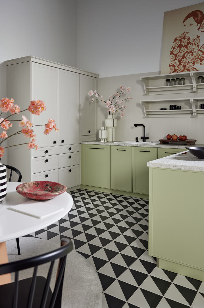 Kitchen with white and light green shaker cabinets, a small island, open shelving, and black and white diamond tile flooring.