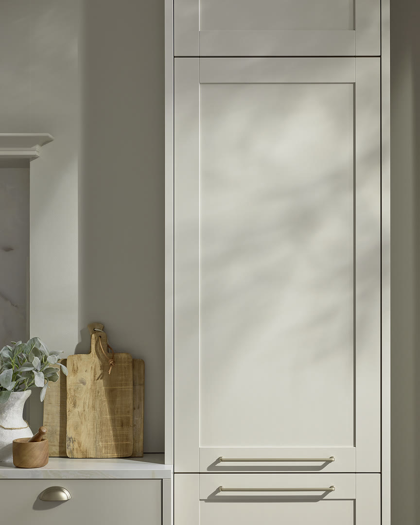 White shaker cabinet doors with recessed panels and brushed metal handles beside an open shelf with a cutting board and plant.