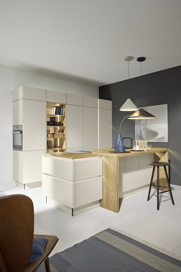 White handleless kitchen with a wood-topped waterfall island, open shelving, pendant lights, and a dark gray accent wall.