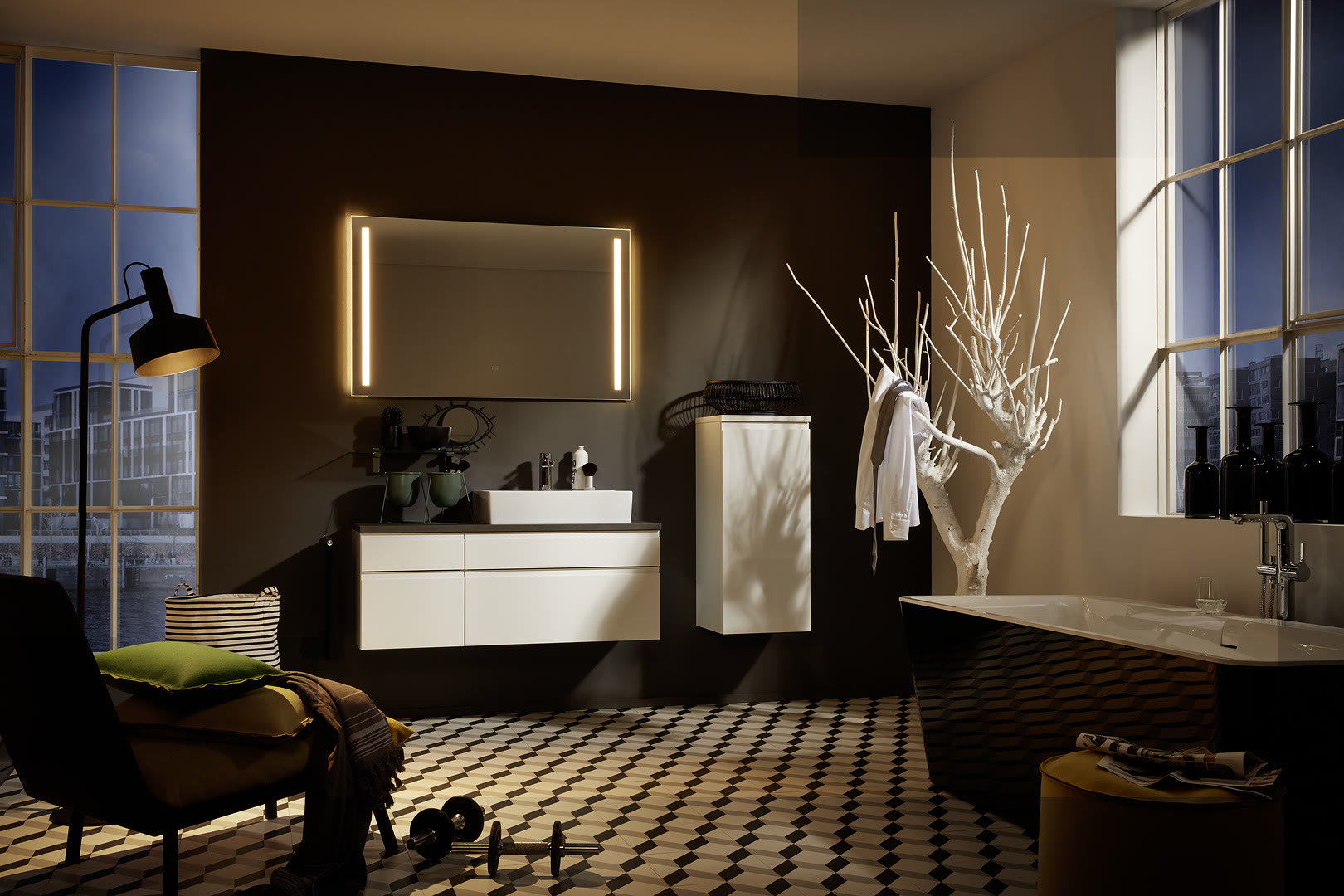White floating vanity and tall white storage unit with an illuminated mirror, freestanding tub, and geometric tile floor