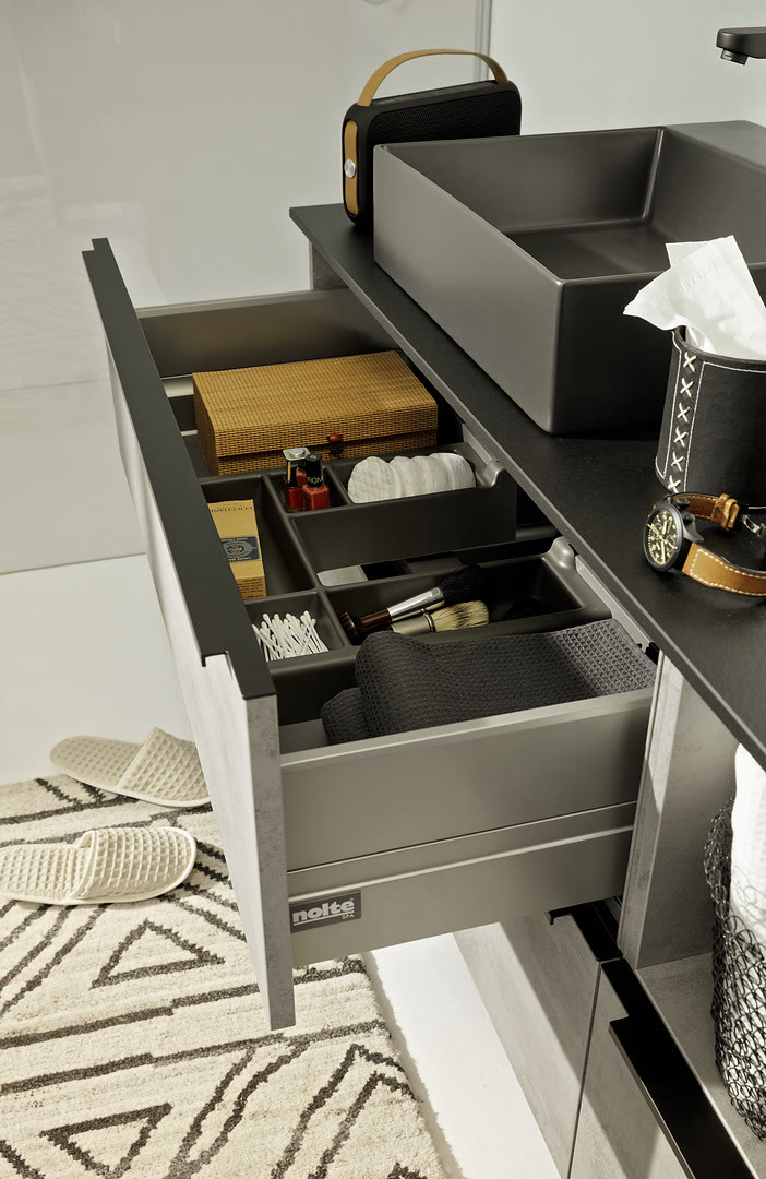 Open white vanity drawer with dividers and organizers holding bathroom accessories beneath a gray stone countertop