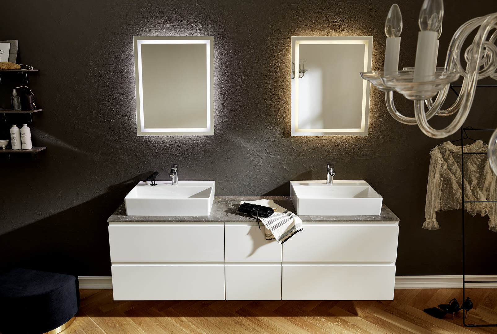 Double-sink vanity with white cabinets, a gray stone counter, two vessel sinks, and two lit mirrors on a dark wall