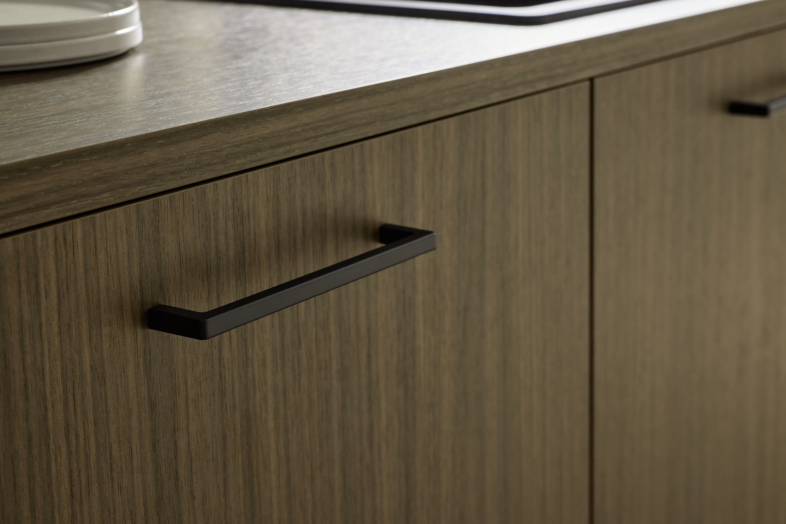 Fluted wood-veneer cabinet fronts in a warm tan tone with a dark stone countertop and black bar handles