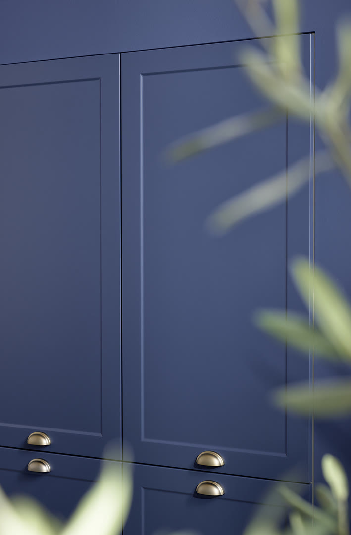 Navy blue shaker-style cabinet fronts with brass cup handles lit by window light