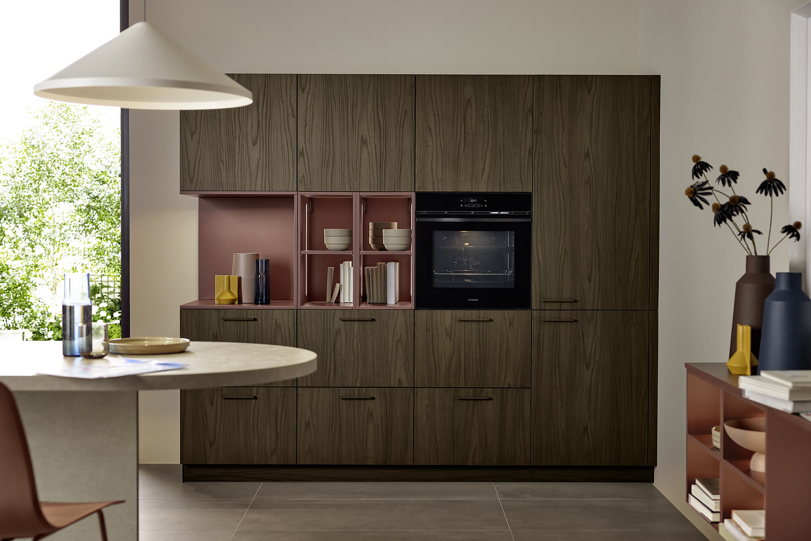 Kitchen with dark wood-grain fronts, a white round waterfall island, and open shelving with a burgundy back