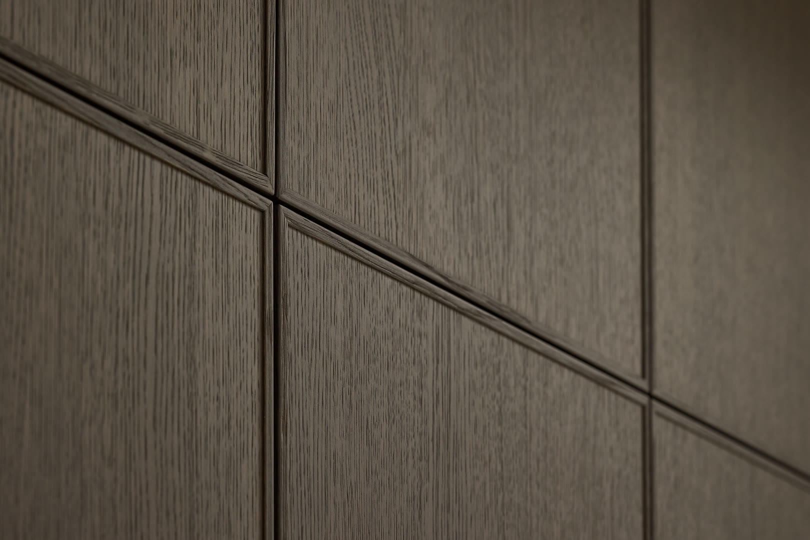Close-up of dark grey wood-grain handleless cabinet fronts with recessed frames and metal edge pulls.