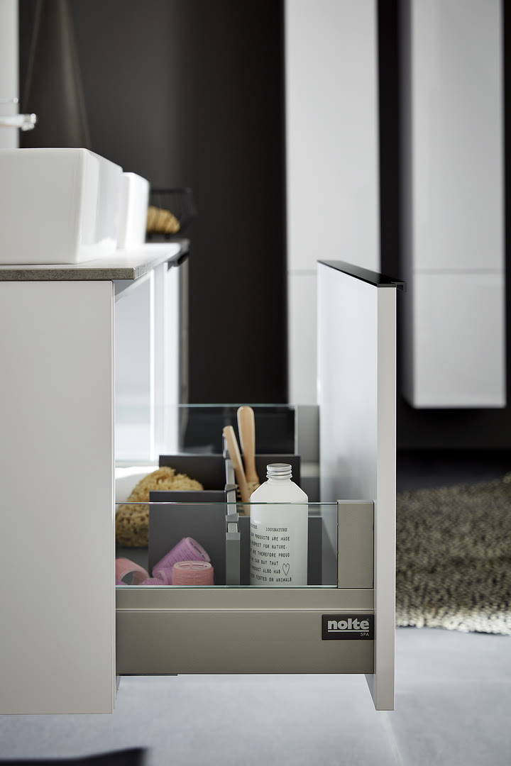 A white cabinet with an open grey internal drawer organizer holding cleaning supplies and utensils under a dark countertop.