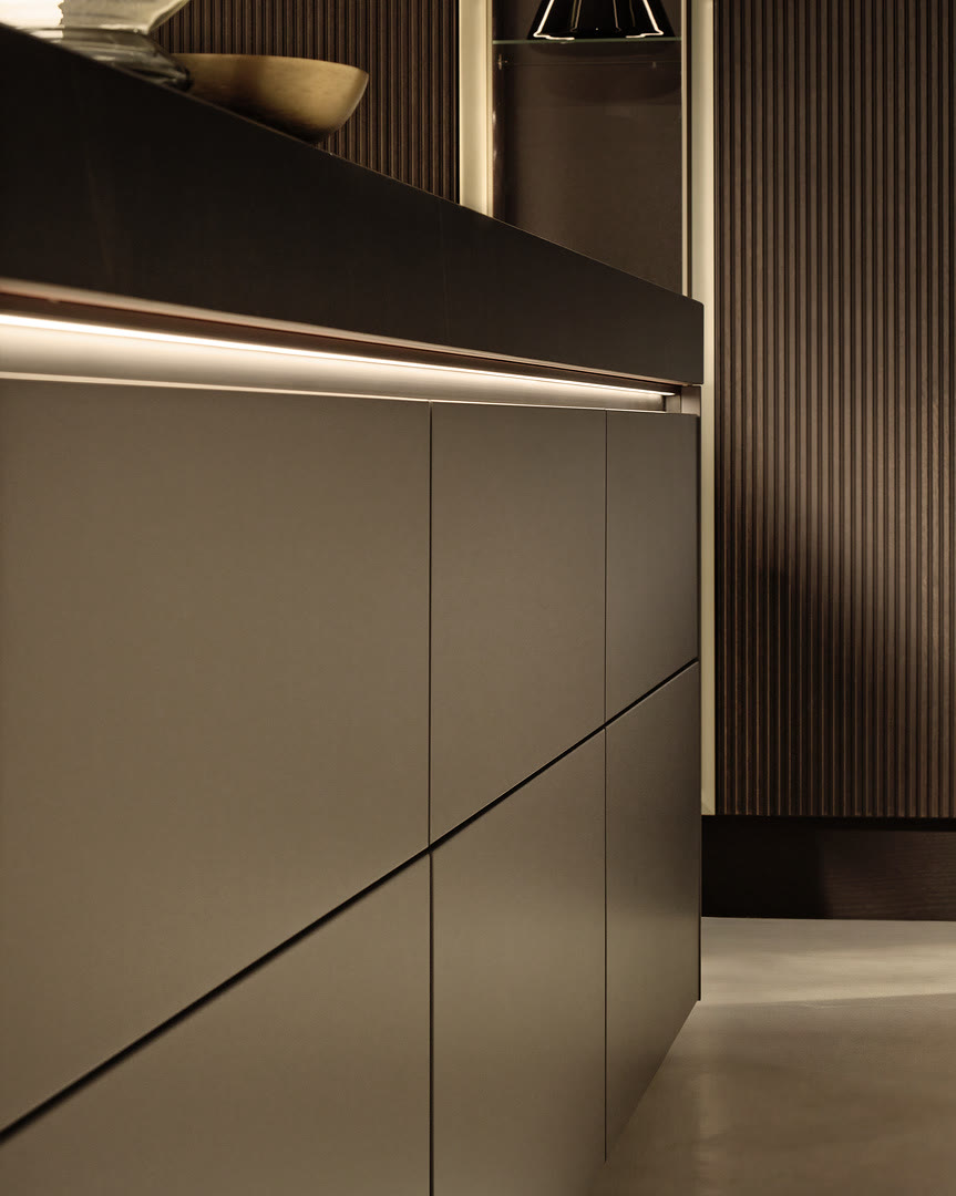 Detail of taupe-grey flat-panel cabinetry with integrated pull handles and a black upper trim with linear lighting.