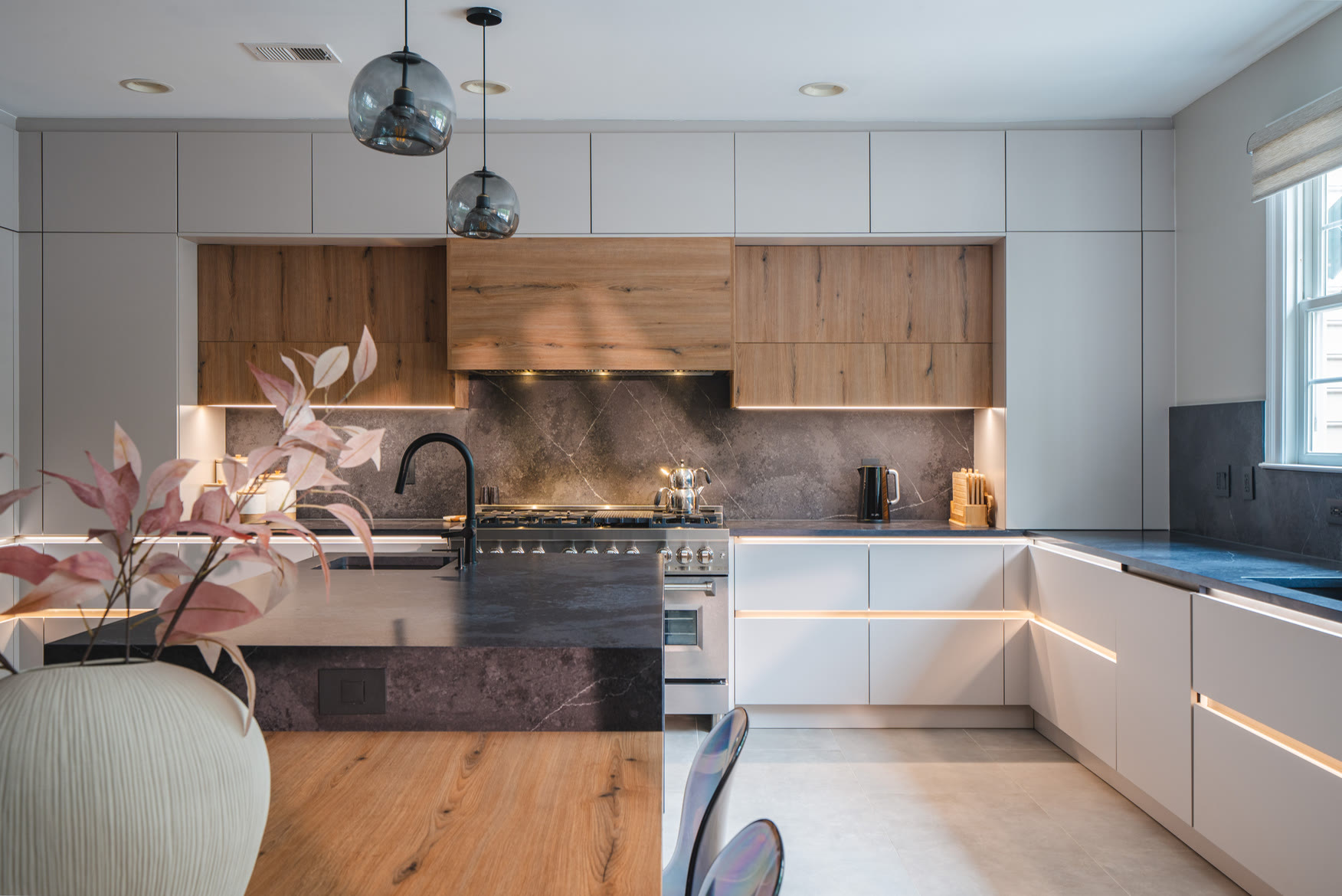 Finished Chantilly kitchen with white lower cabinets, natural wood upper cabinets, a dark stone waterfall island and pendant lights.