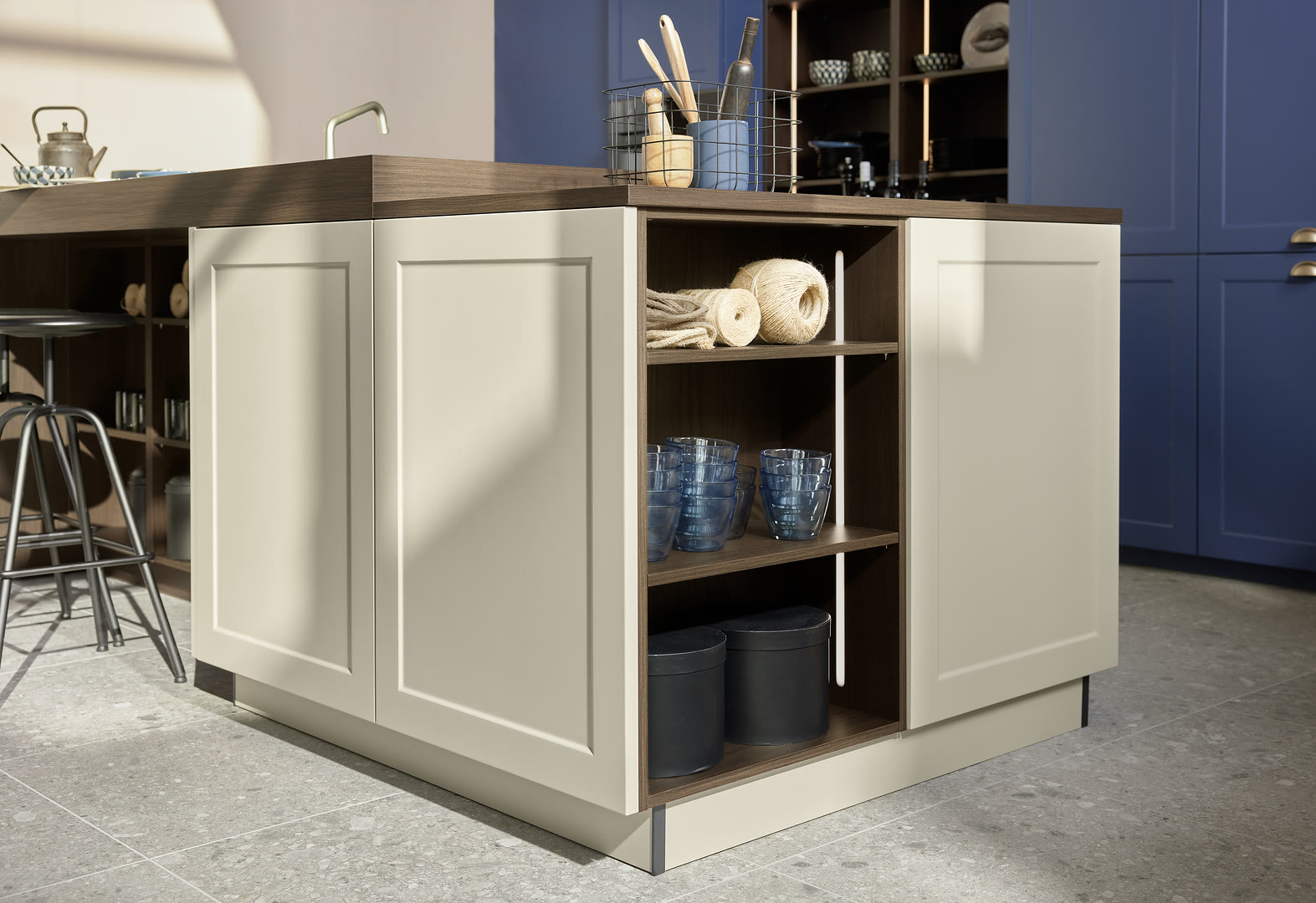 Cream island with open shelving and recessed panel doors next to navy blue wall cabinets