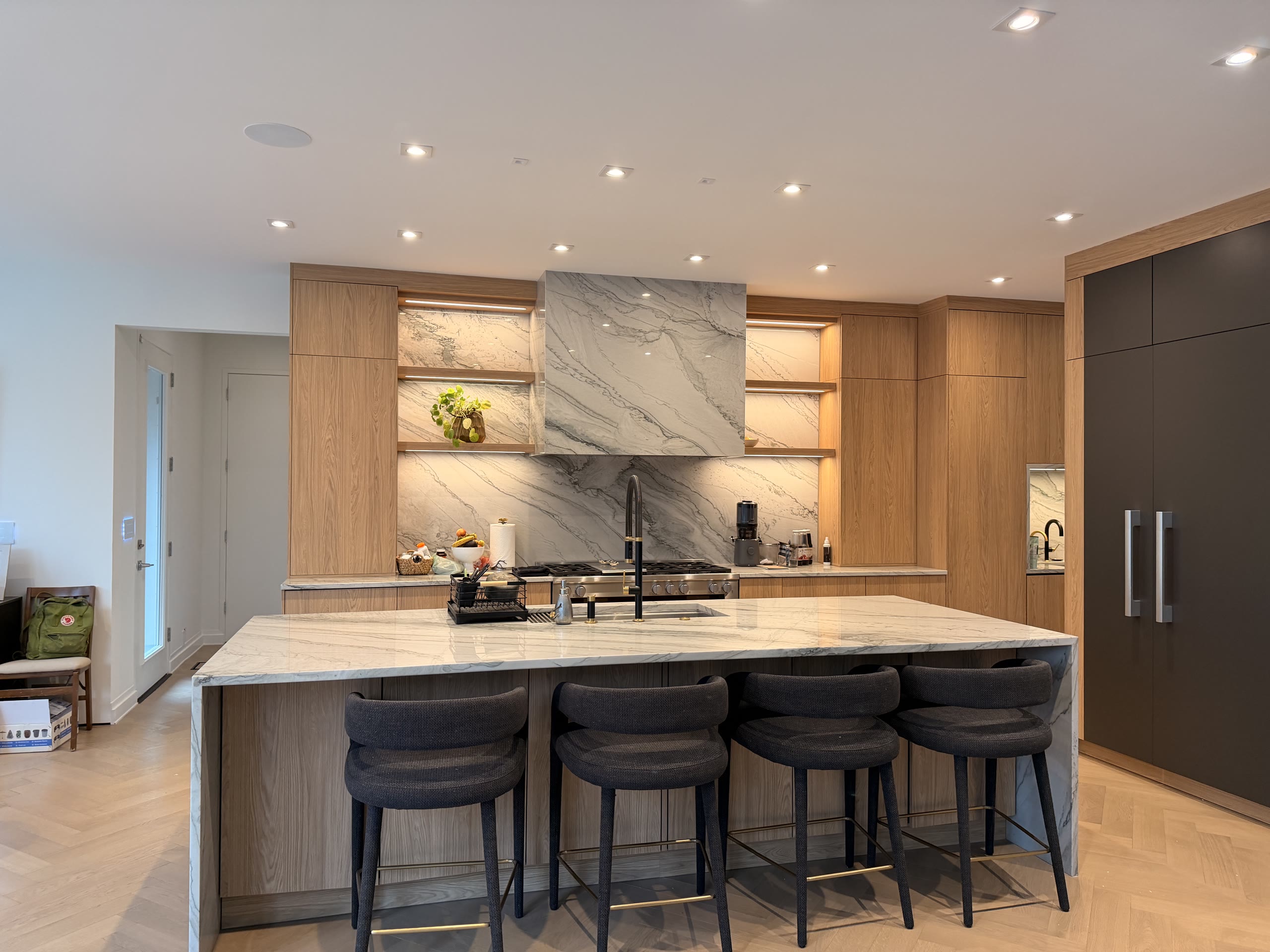 A finished kitchen with light wood cabinets, a waterfall marble island, and black bar seating.