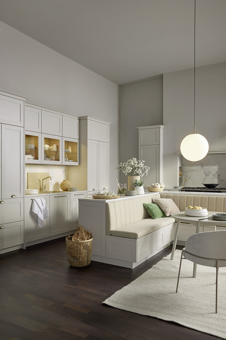 Open-plan kitchen with white shaker cabinetry, glass-front upper cabinets, and banquette seating.