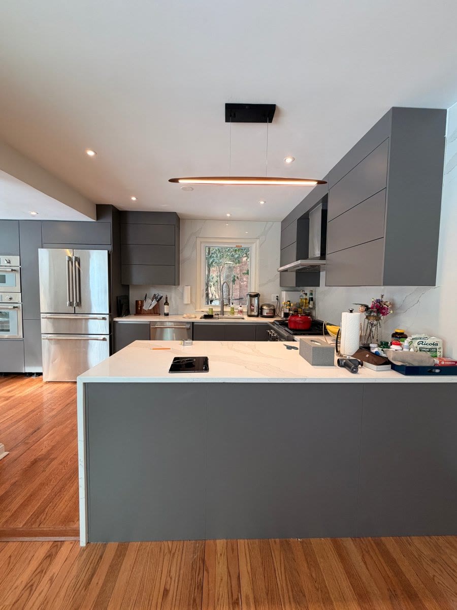 Finished kitchen with gray handleless cabinets, a white quartz island, and a brass linear pendant.