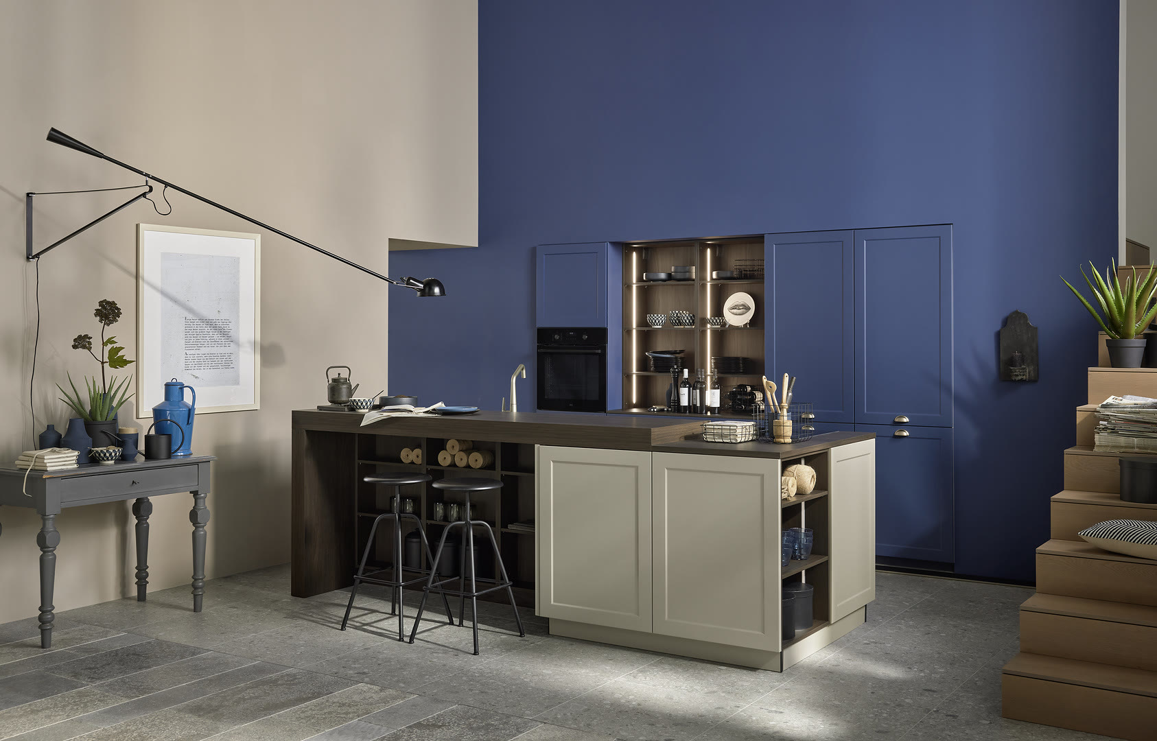 Two-tone kitchen with a cream and black island, blue glass-front wall cabinets, and black stools.